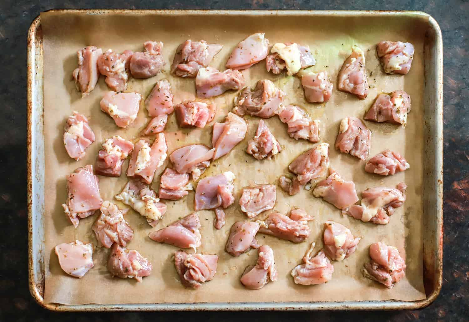 sheet pan with parchment paper and raw chicken pieces.