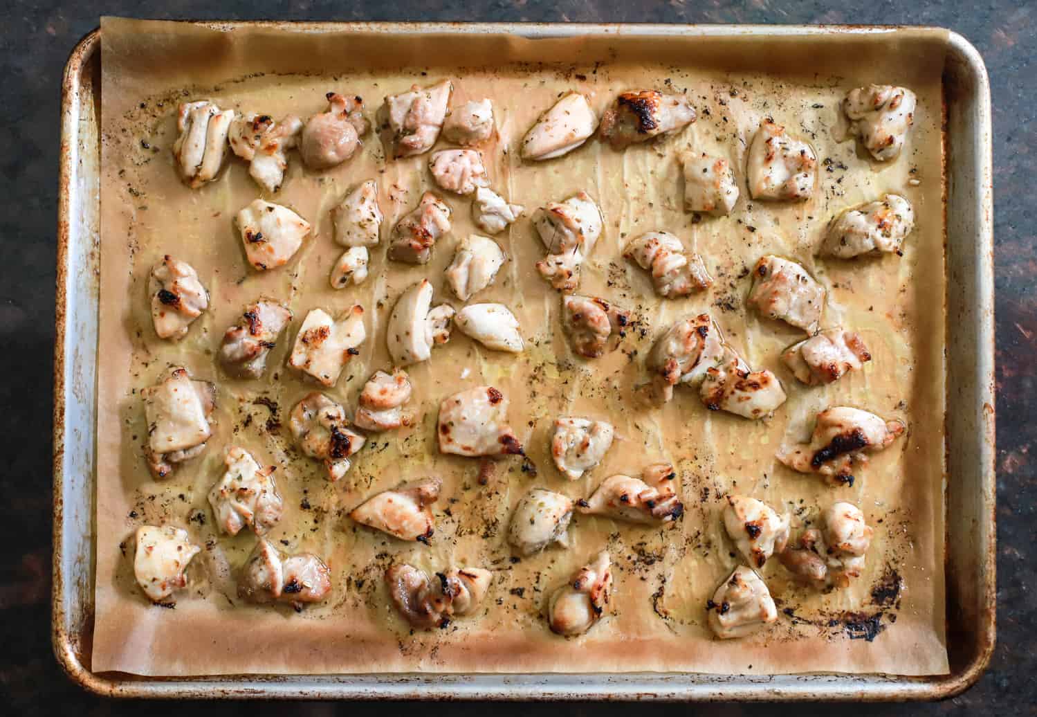 sheet pan of honey lemon chicken thigh pieces broiled with oregano.