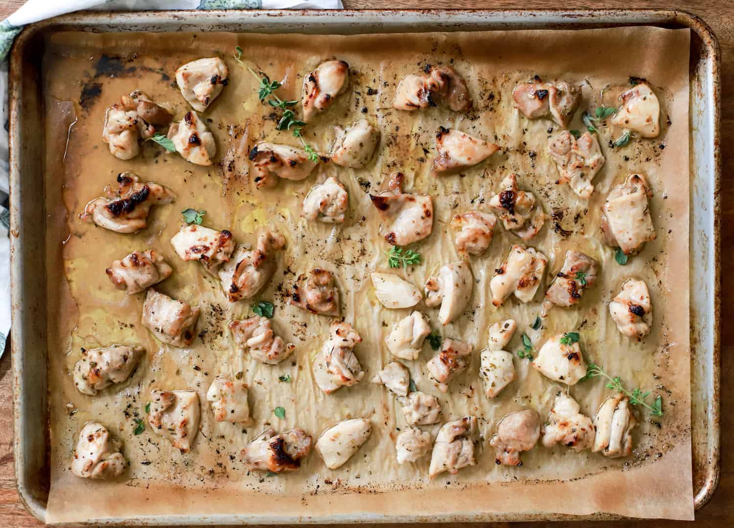 sheet pan with broiled chicken bites topped with oregano.