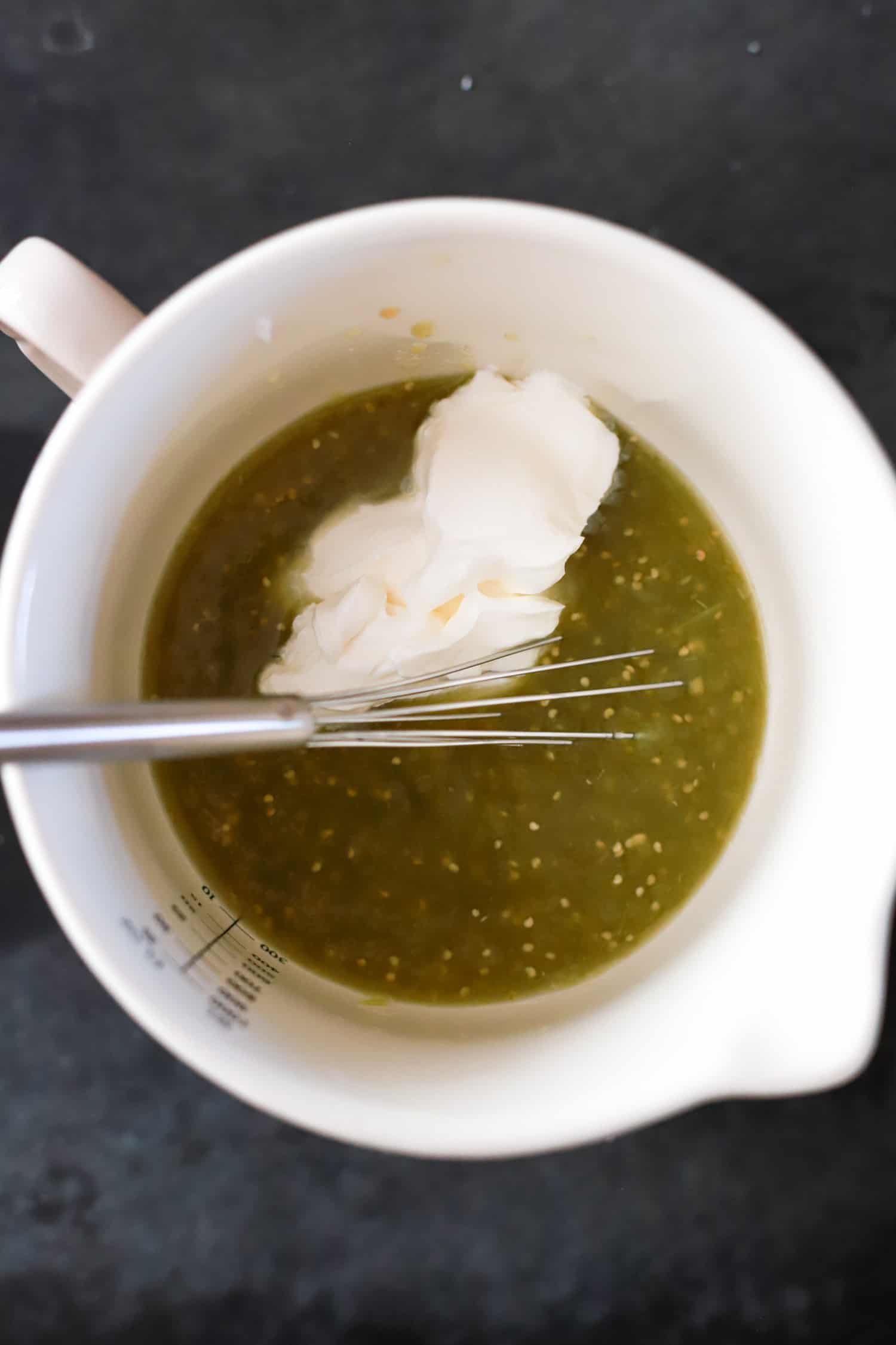 Bowl with verde sauce and sour cream plus a small whisk for sauce.