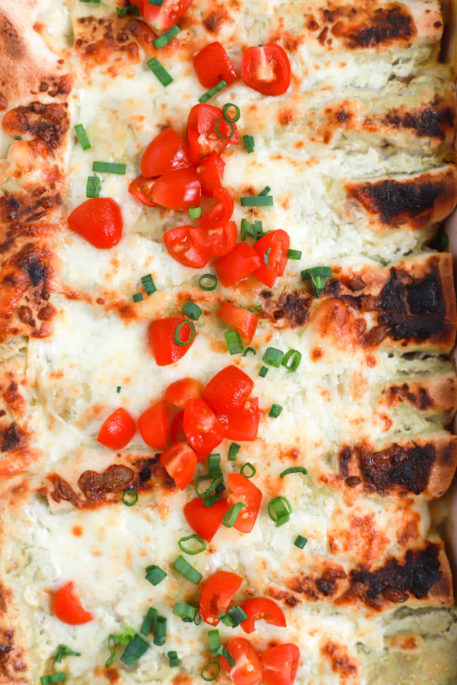 Close up top view of enchiladas topped with fresh tomatoes and green onions.