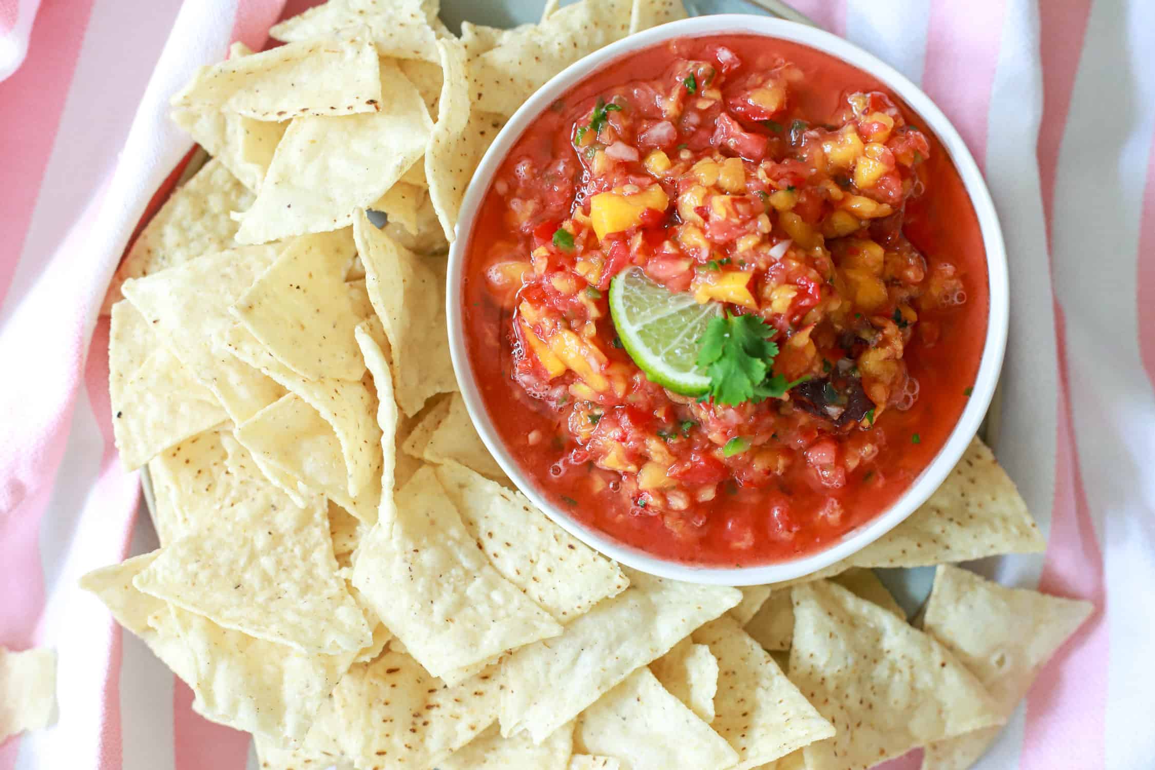 White bowl of peach salsa with tortilla chips surrounding it.
