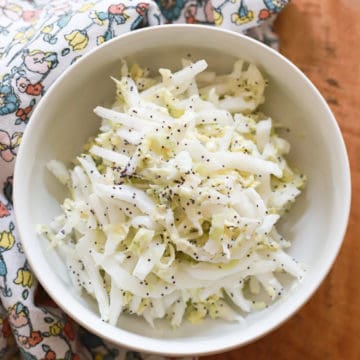 white bowl of poppyseed slaw with Greek yogurt on wooden board with floral napkin.