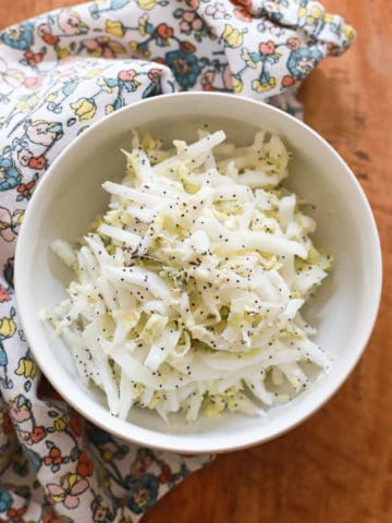 white bowl of poppyseed slaw with Greek yogurt on wooden board with floral napkin.