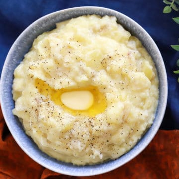 roasted garlic mashed potatoes with a pat of butter on top in a blue bowl on linens.