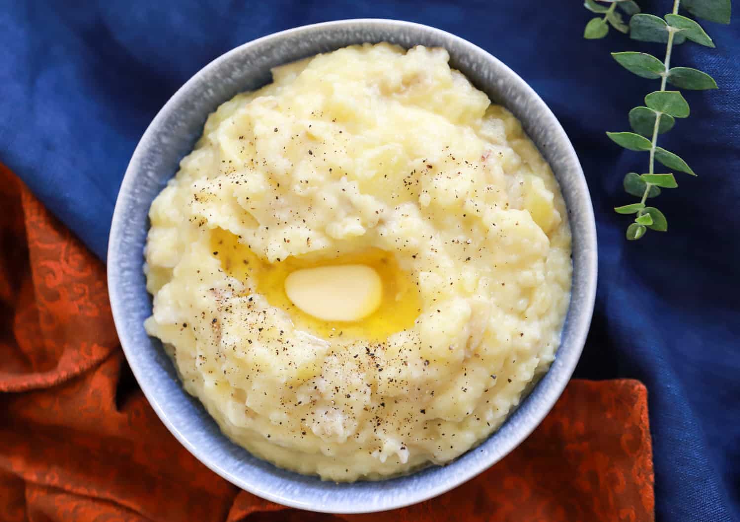 roasted garlic mashed potatoes with a pat of butter on top in a blue bowl on linens.