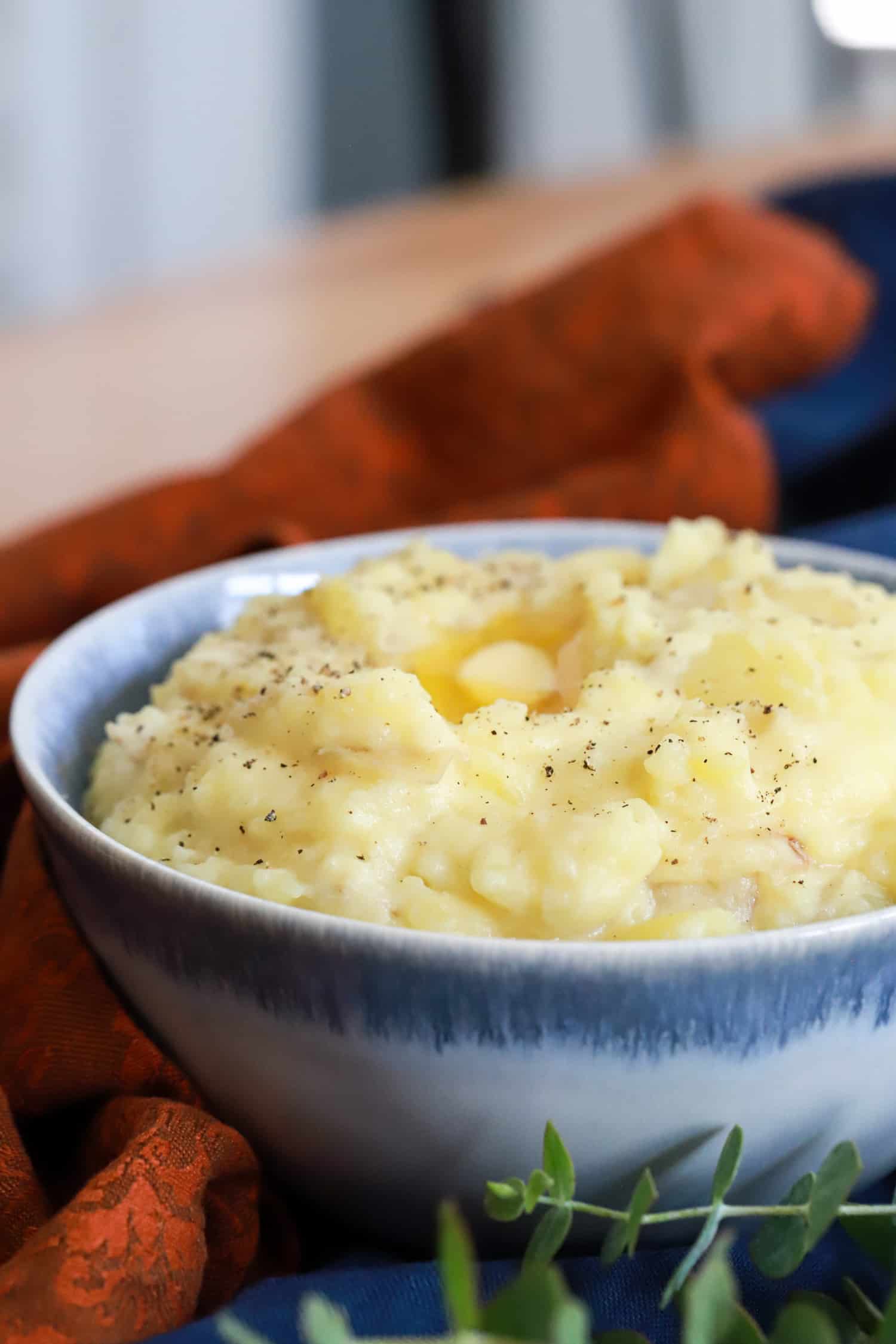 side view bowl of mashed potatoes with burnt orange napkin in background.