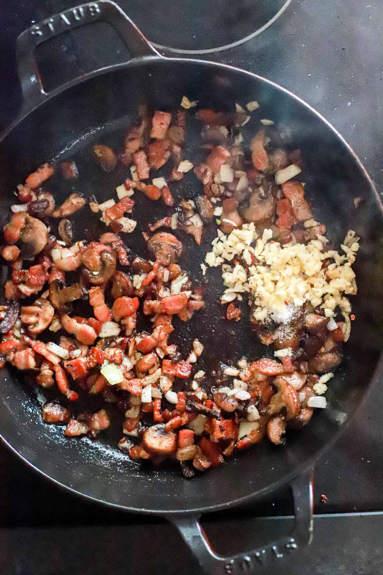 black skillet with mushrooms, bacon, and garlic.