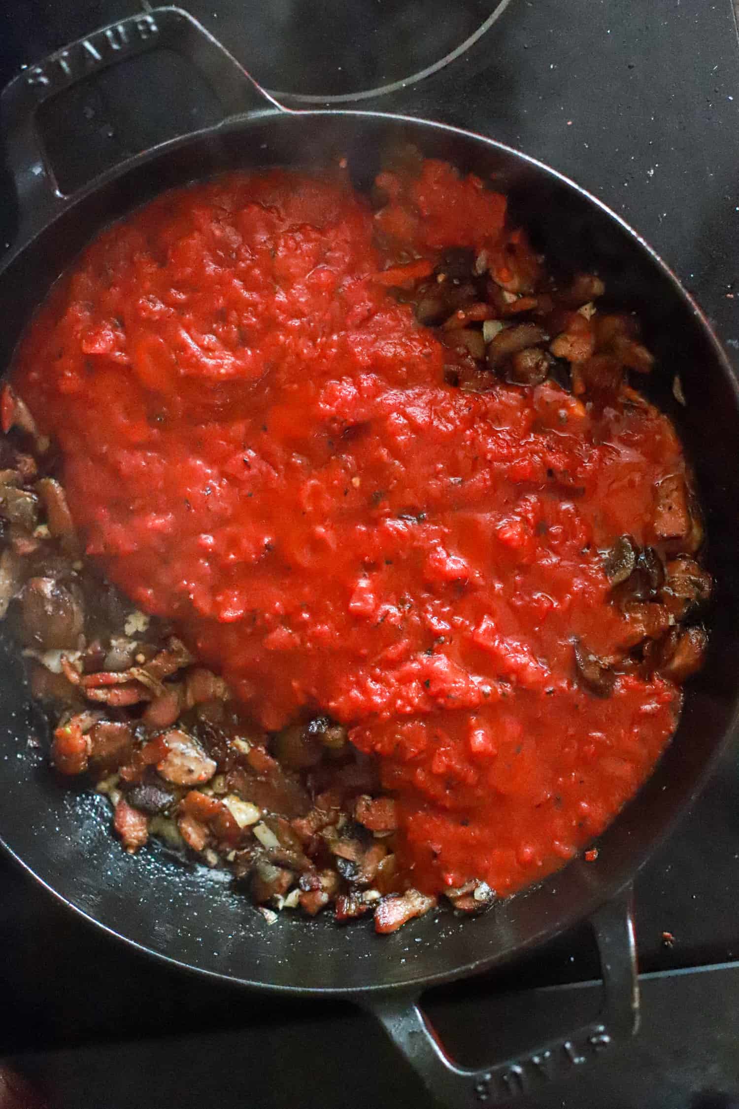 black skillet with tomatoes and mushrooms for spaghetti sauce.
