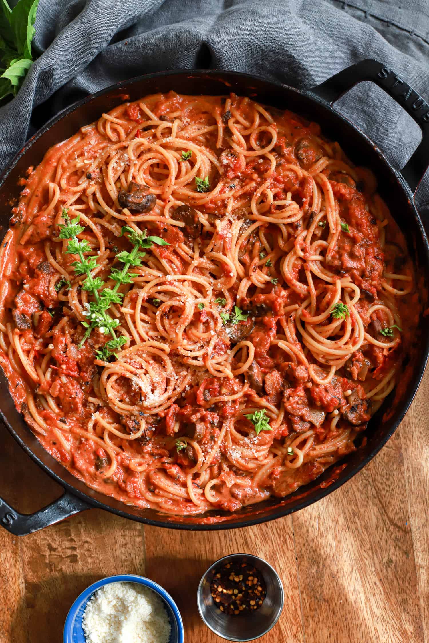 black skillet of mushroom bacon spaghetti with basil leaves on top.