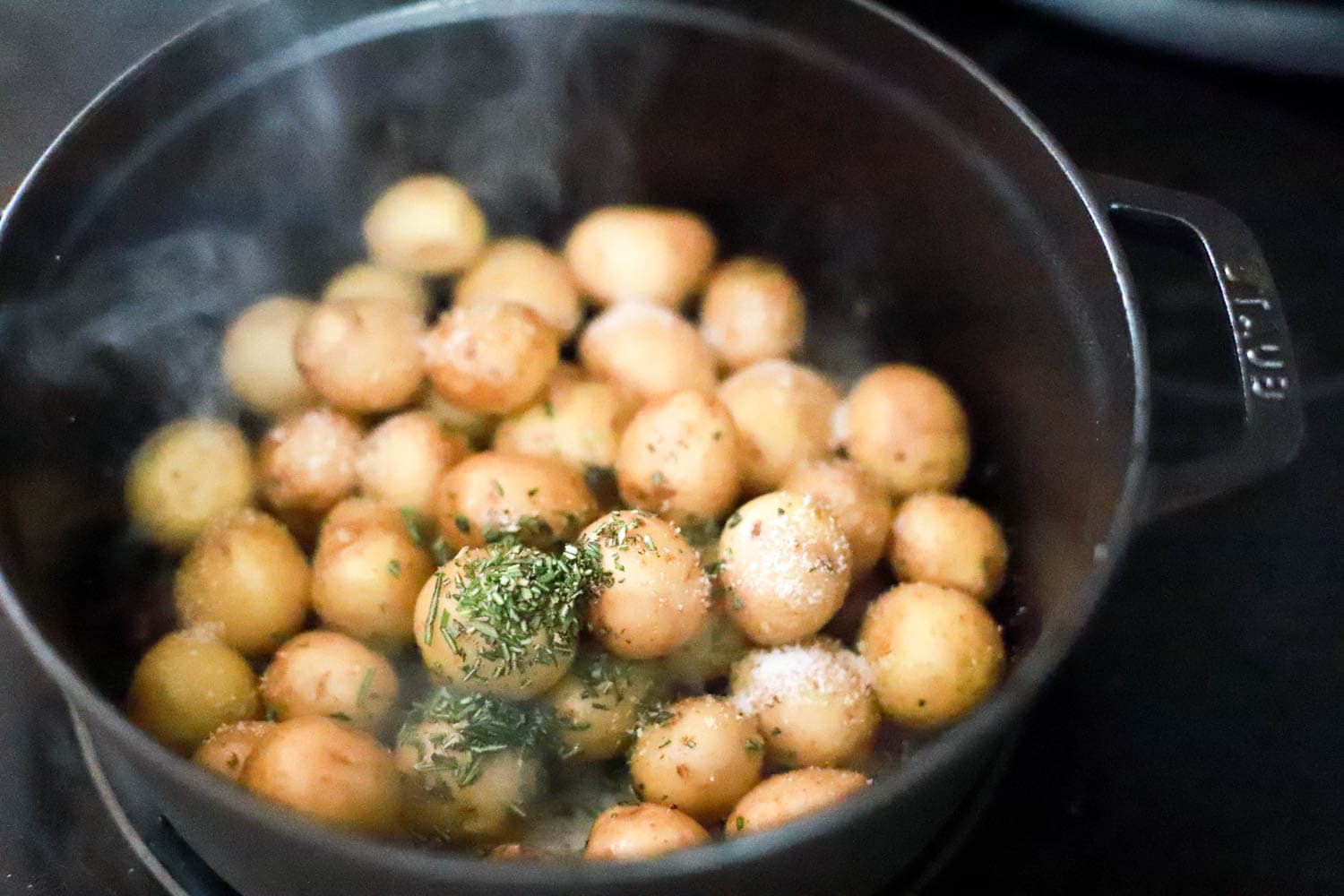 Black cast iron pot with new potatoes, salt, and chopped rosemary leaves.