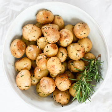 Steamed small yukon gold potatoes with rosemary in a large white bowl.