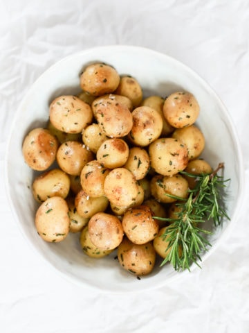 Steamed small yukon gold potatoes with rosemary in a large white bowl.