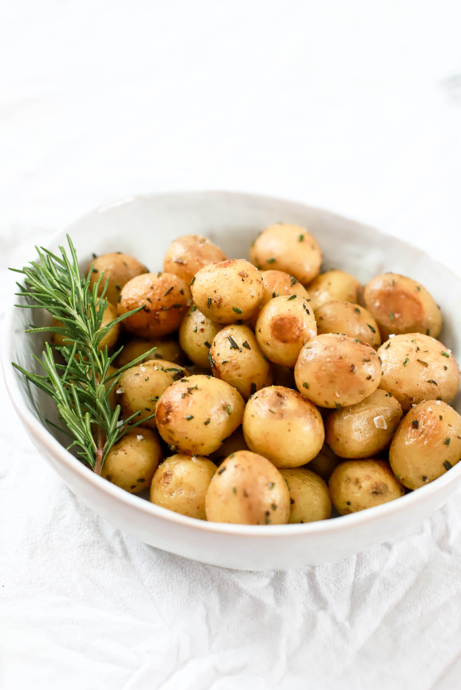 White bowl of steamed baby potatoes with rosemary.