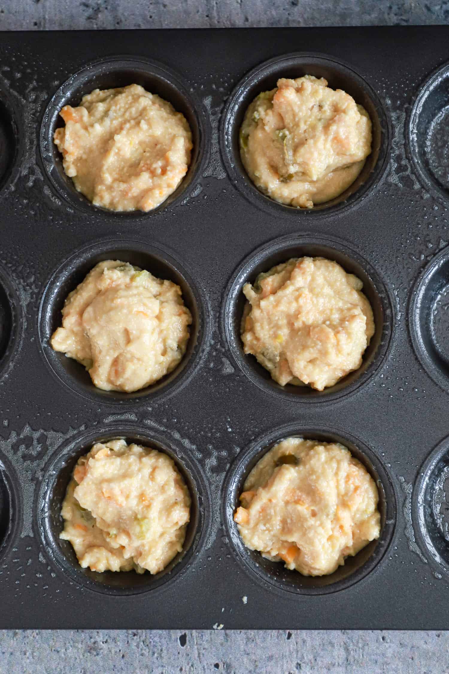 close up of cornbread muffin batter unbaked in black nonstick muffin pan.