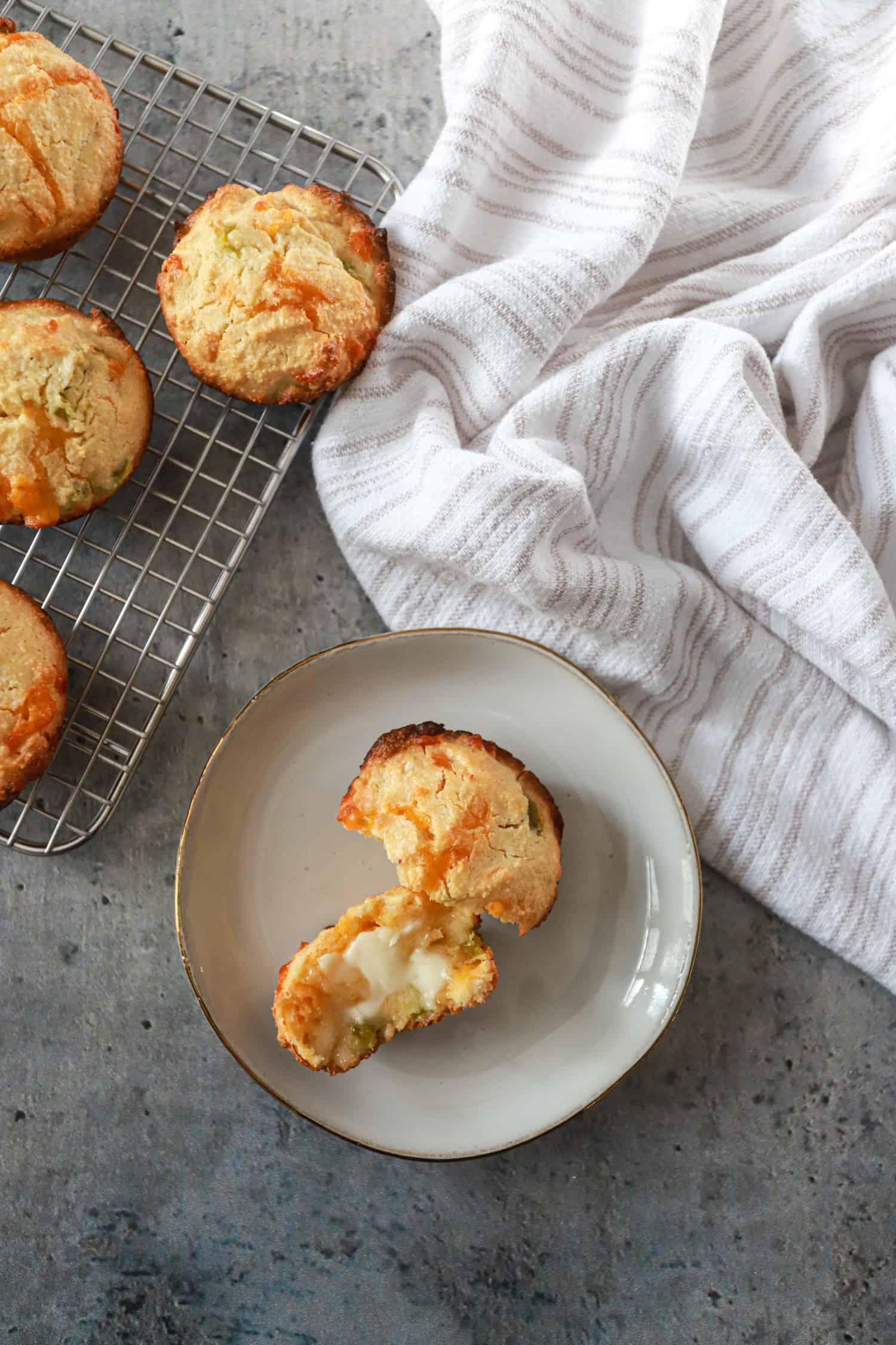 corn muffins on wire rack with one on a small white plate broken and spread with butter.