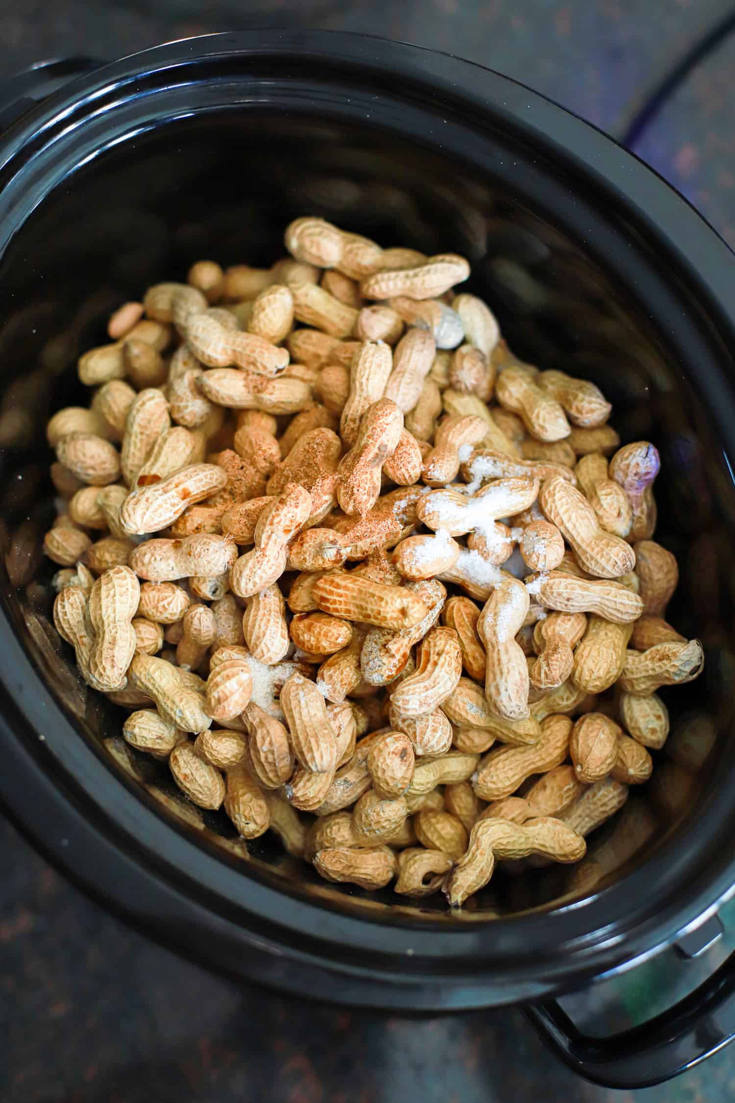 Black slow cooker with raw peanuts and seasonings.