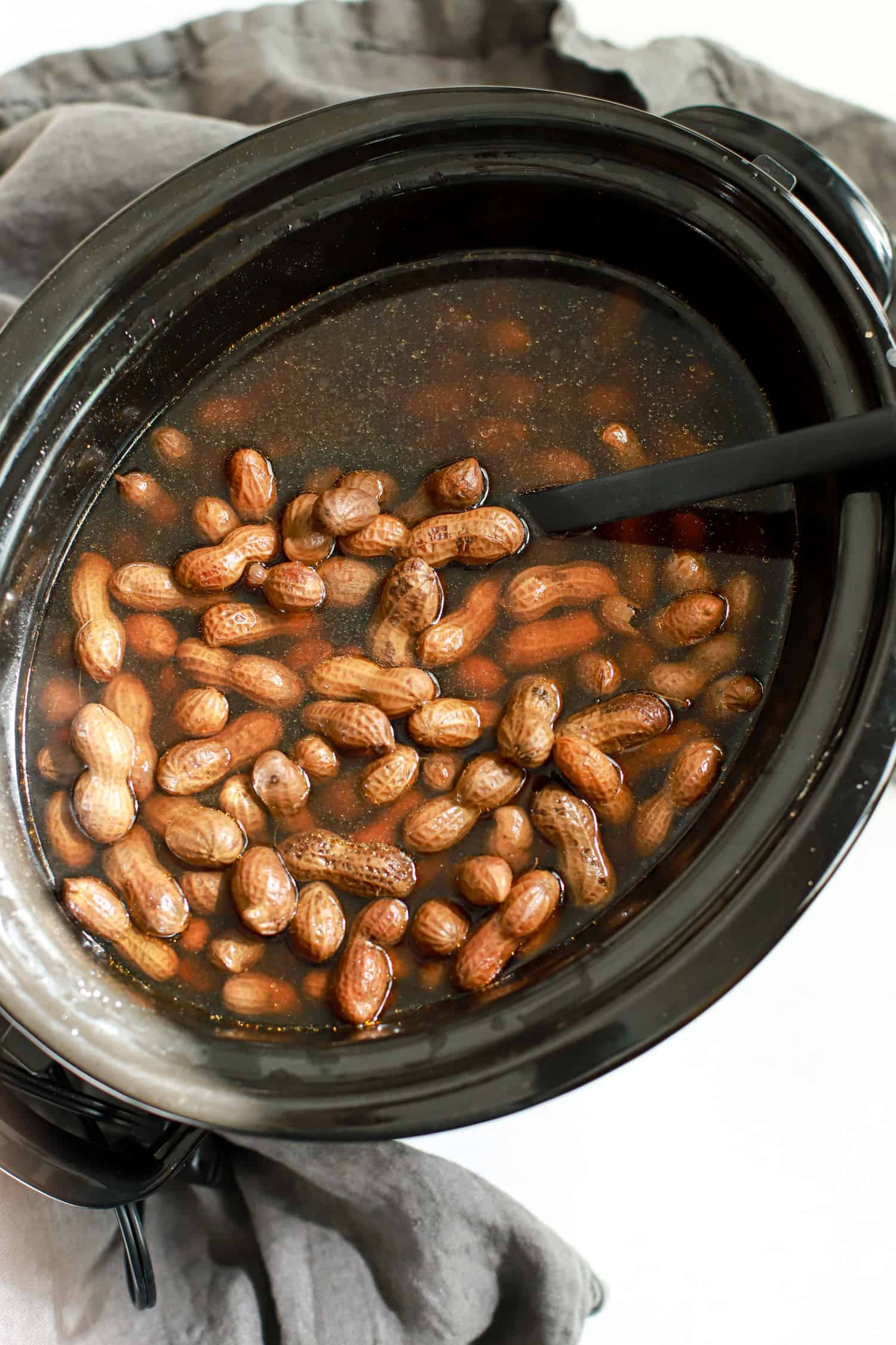Slow cooker holding boiled peanuts with a black spoon.