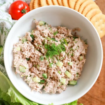 Large white bowl of tuna salad surrounded by crackers and decorative napkin.