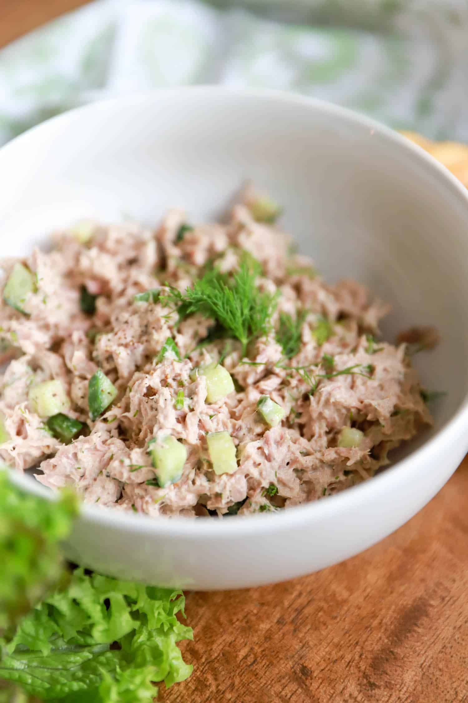 Side view of white bowl with cucumber tuna salad topped with fresh dill.