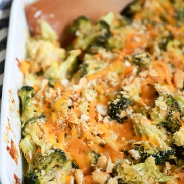 white baking dish of broccoli cheddar casserole with wooden spoon.