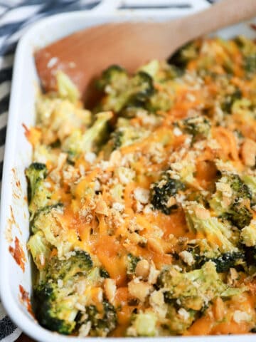 white baking dish of broccoli cheddar casserole with wooden spoon.