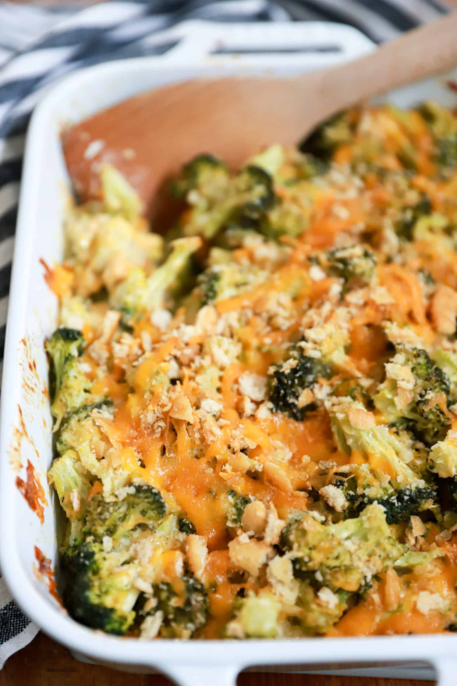 white baking dish of broccoli cheddar casserole with wooden spoon.