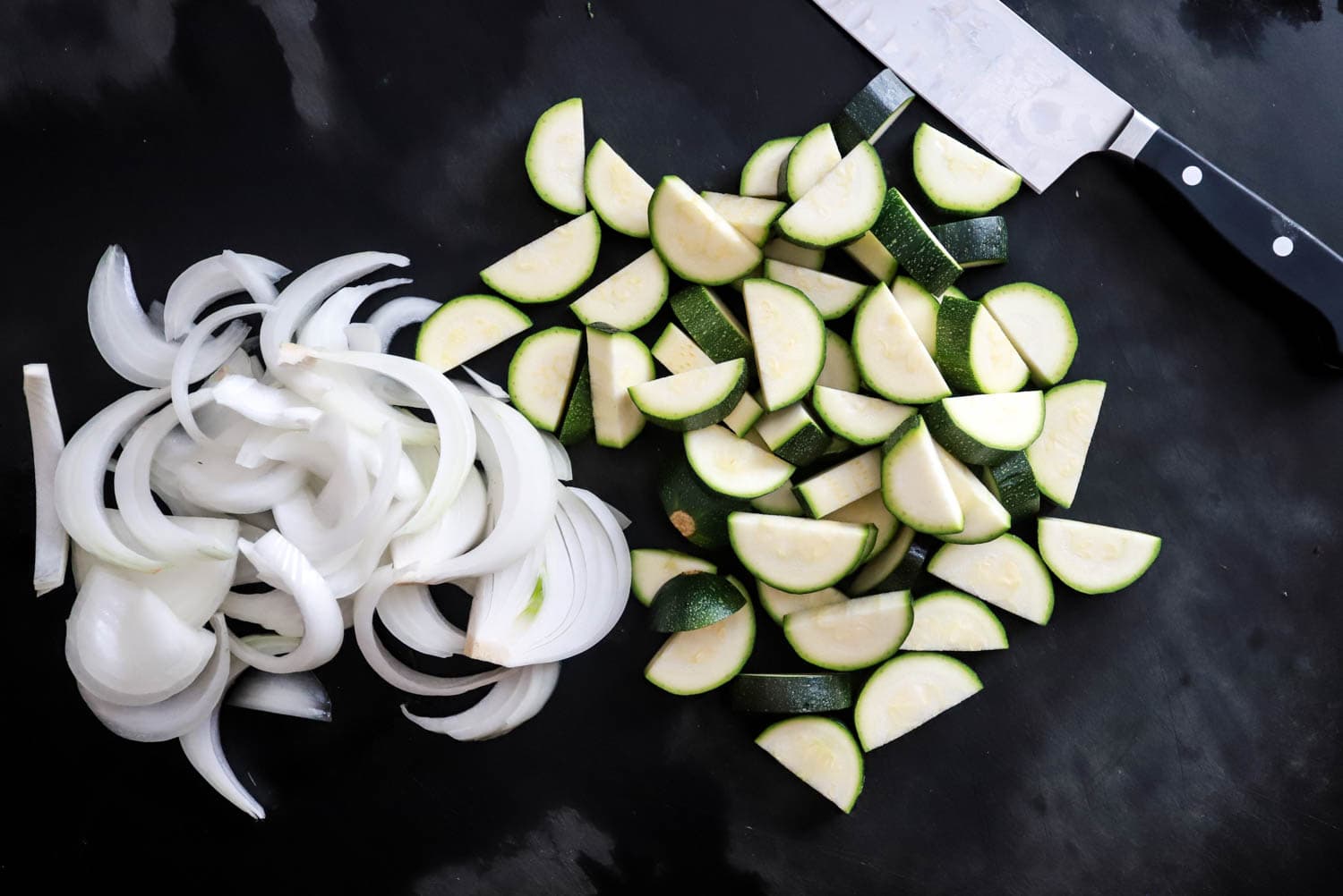 raw zucchini and onions cut up on black board.