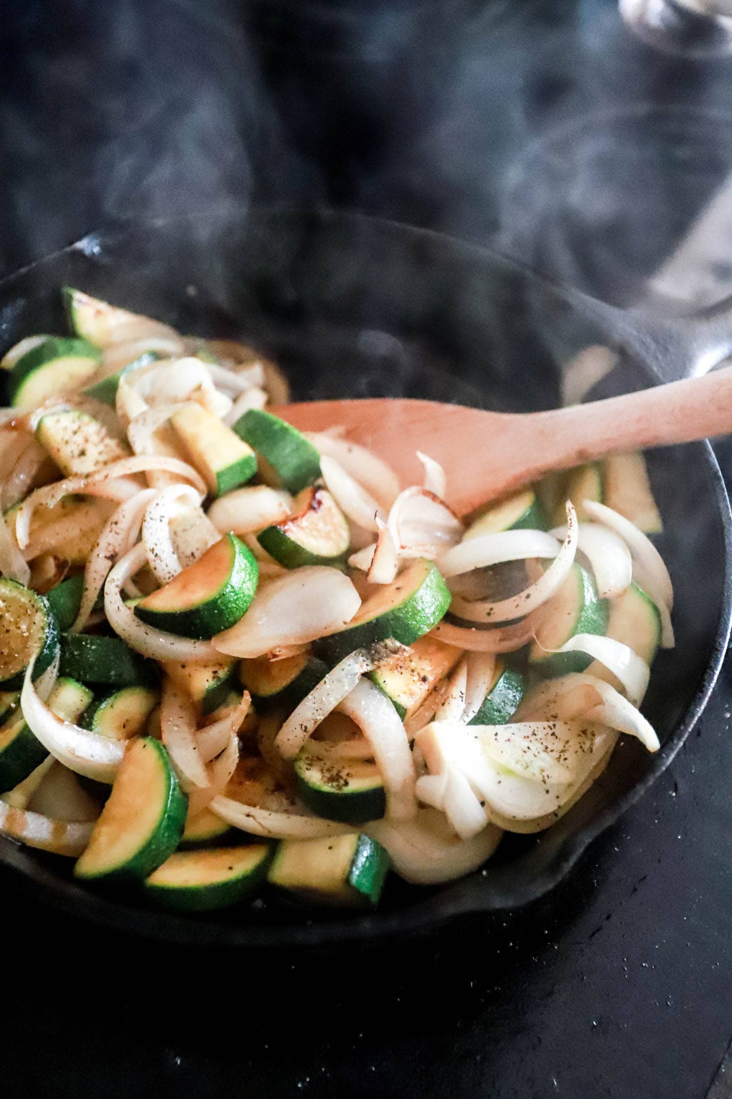 Black skillet of sizzling veggies with black pepper on top.