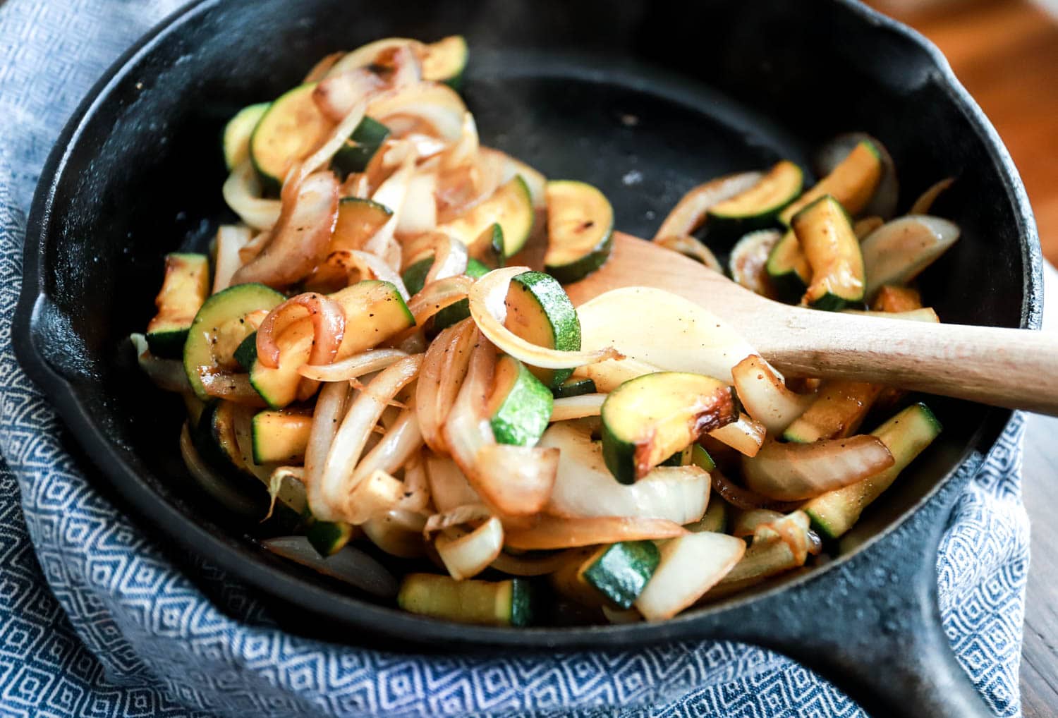 Zucchini and onions in a skillet with blue napkin on the outside.