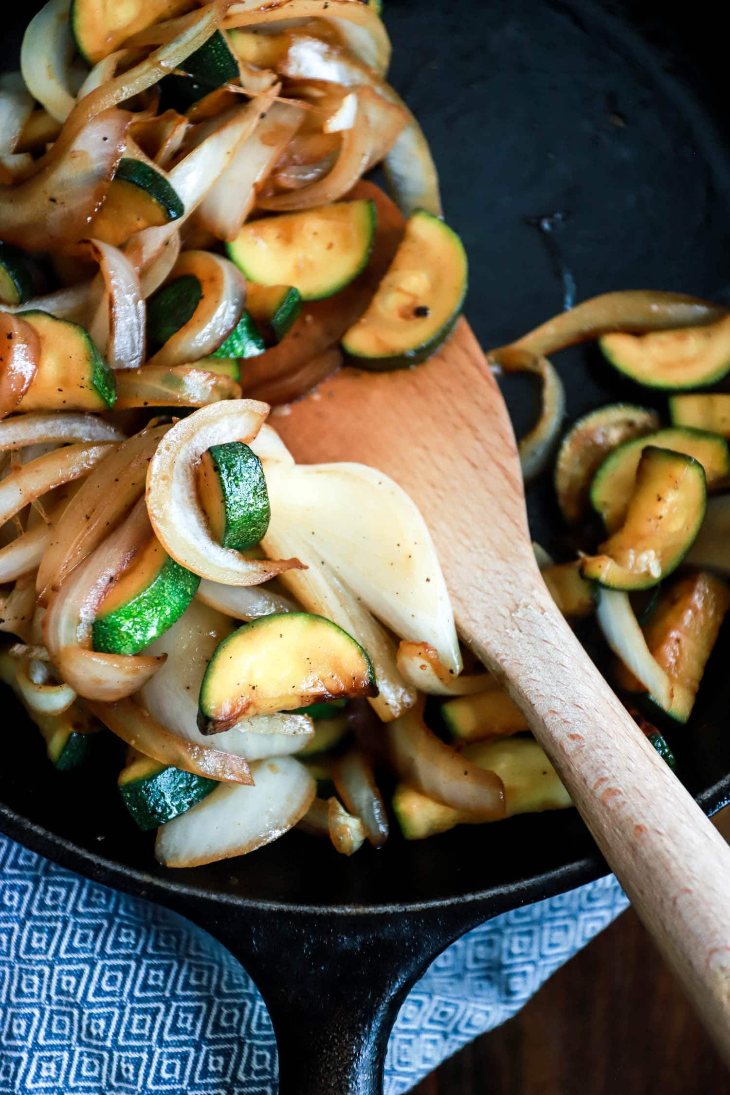 Close up sauteed zucchini and onions with wooden paddle spoon.