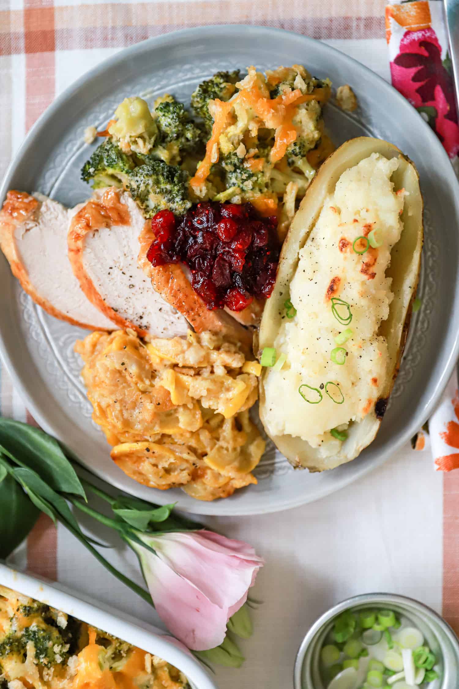 Thanksgiving plate with turkey, cranberry sauce, squash and broccoli casseroles, and half a twice baked potato on a ceramic gray plate.