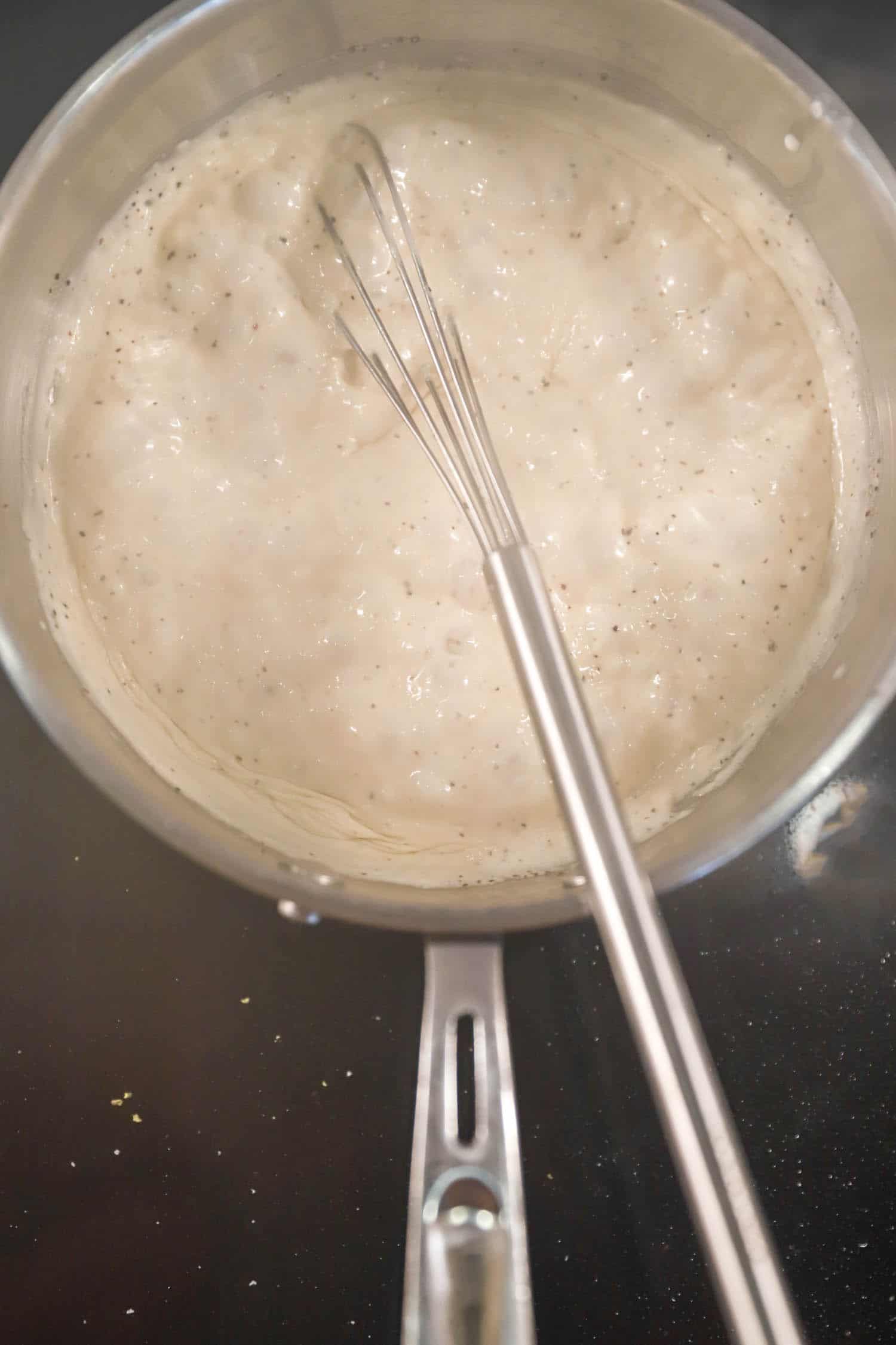 Small pan of cream sauce with thin whisk.