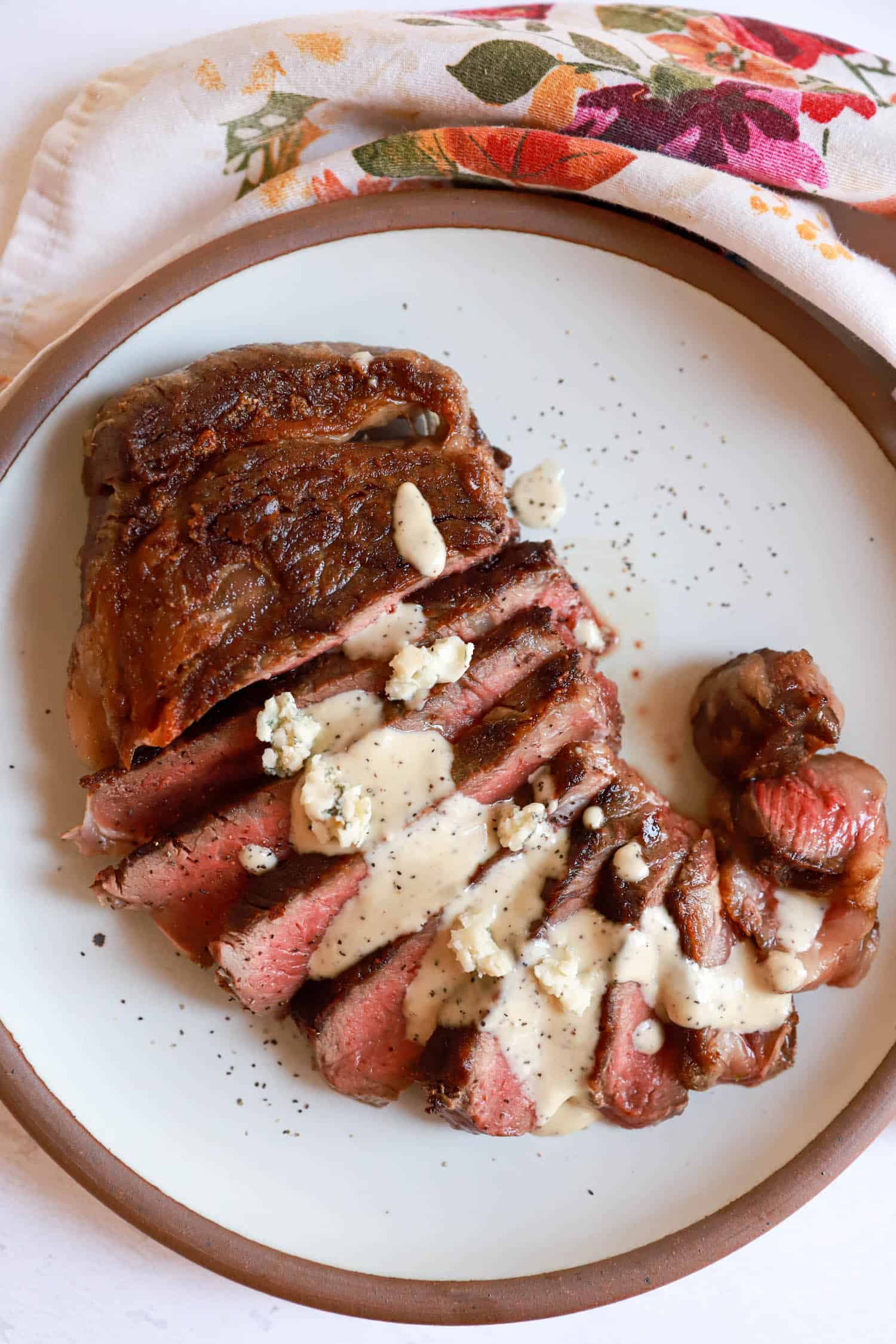 Round ceramic plate with sliced rare steak topped with gorgonzola sauce.