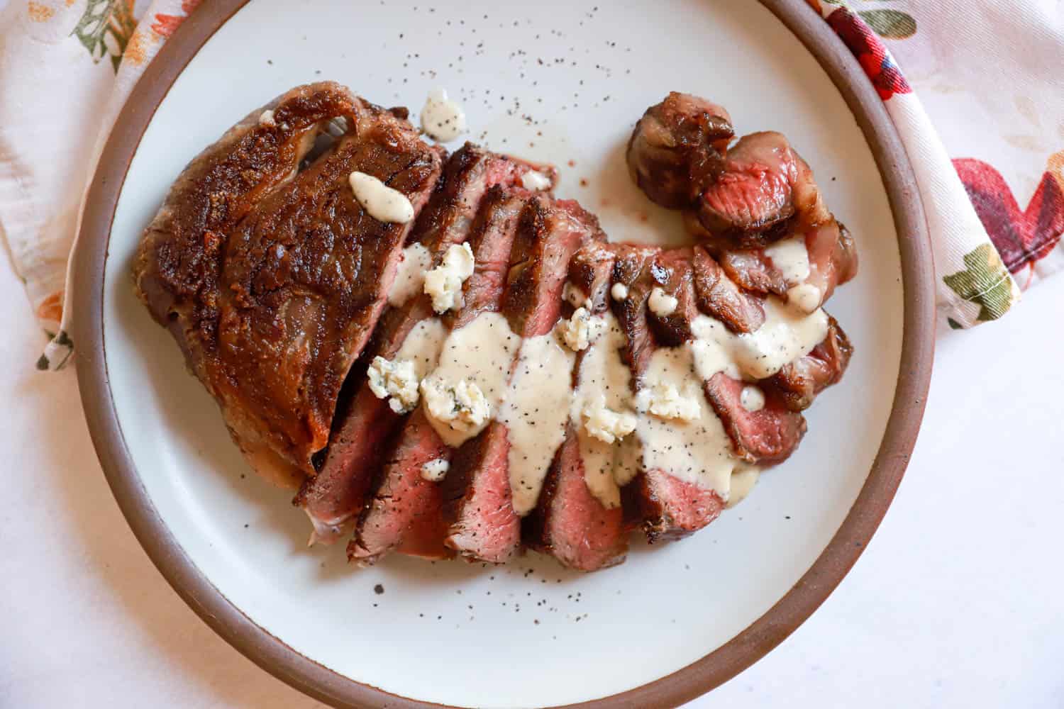Round plate of sliced ribeye with gorgonzola sauce drizzled over top.