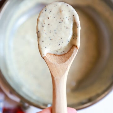 Small wooden spoon with gorgonzola cream sauce held over small saucepan.