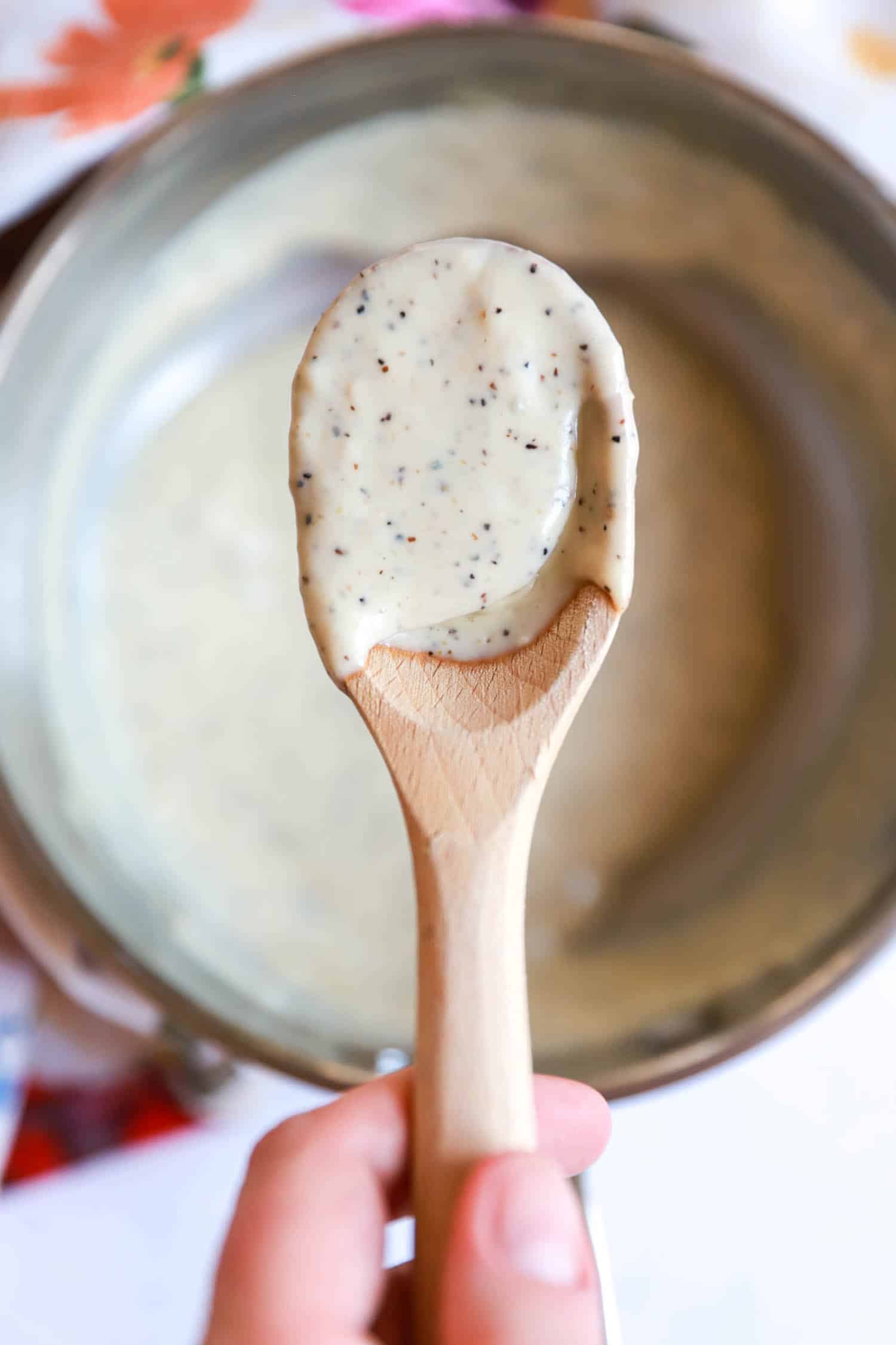 Small wooden spoon with gorgonzola cream sauce held over small saucepan.
