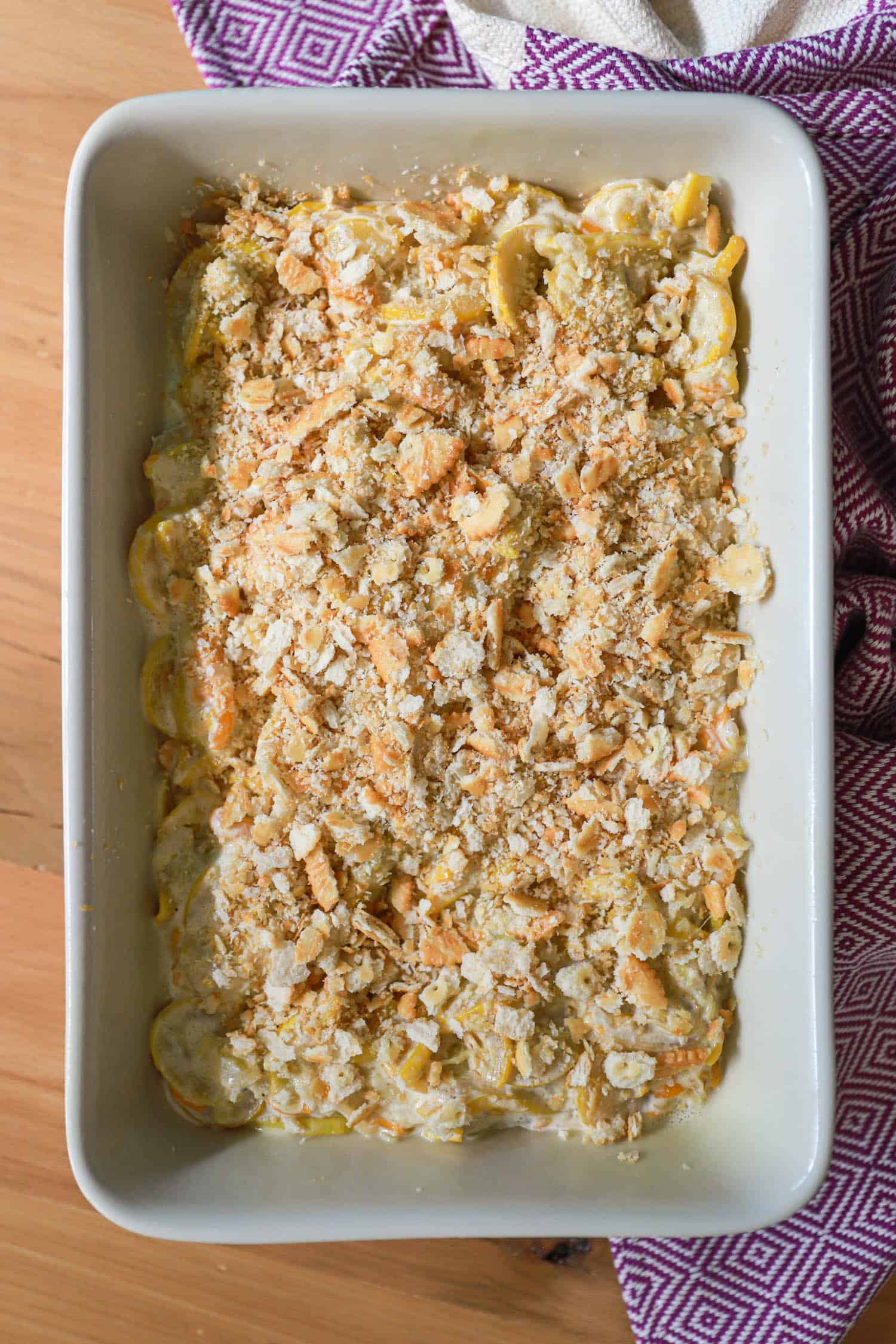 Large dish of unbaked squash casserole with crumbled Ritz crackers on top.
