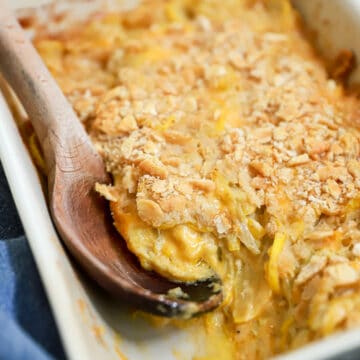 Side angle view of squash casserole with a wooden spoon scooping into the baking dish.