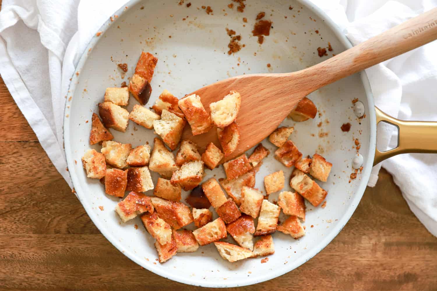 skillet with wooden paddle and croutons on white napkin.