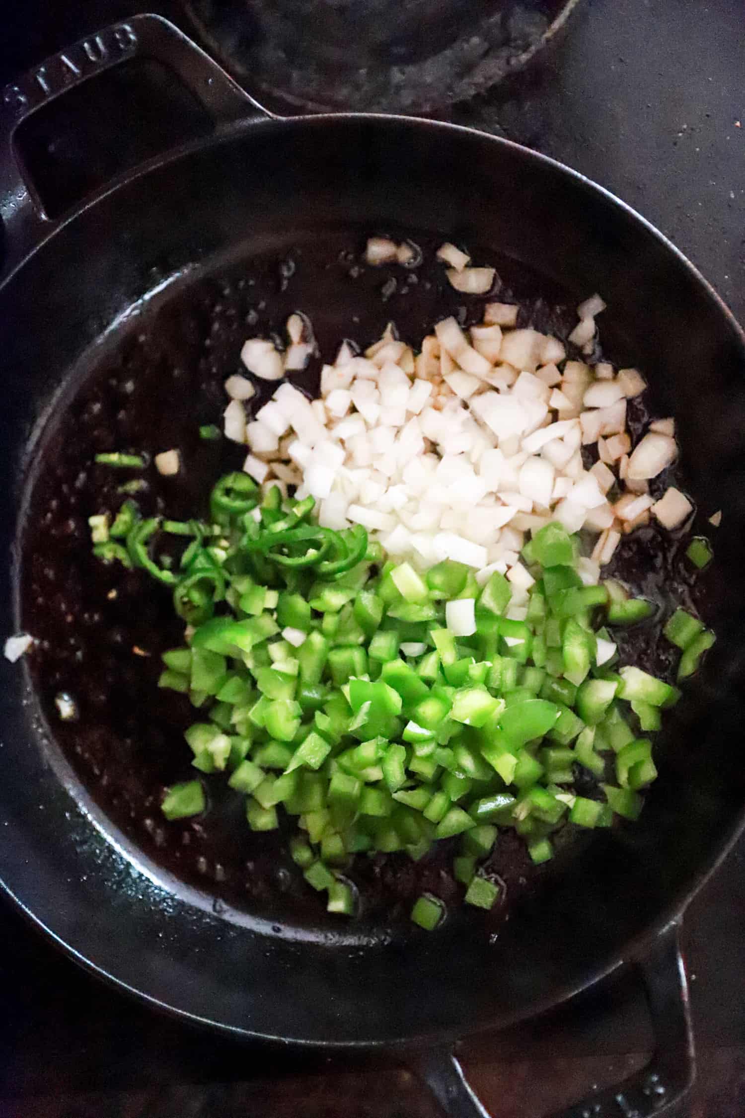 onions and green peppers browning in black skillet.