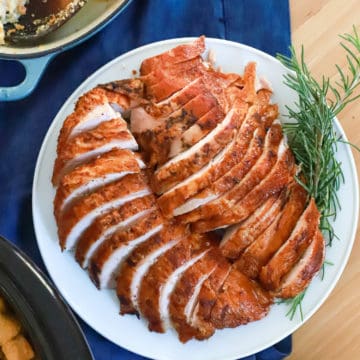 plate of sliced smoked turkey with rosemary garnish on navy blue napkin.