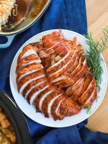 plate of sliced smoked turkey with rosemary garnish on navy blue napkin.