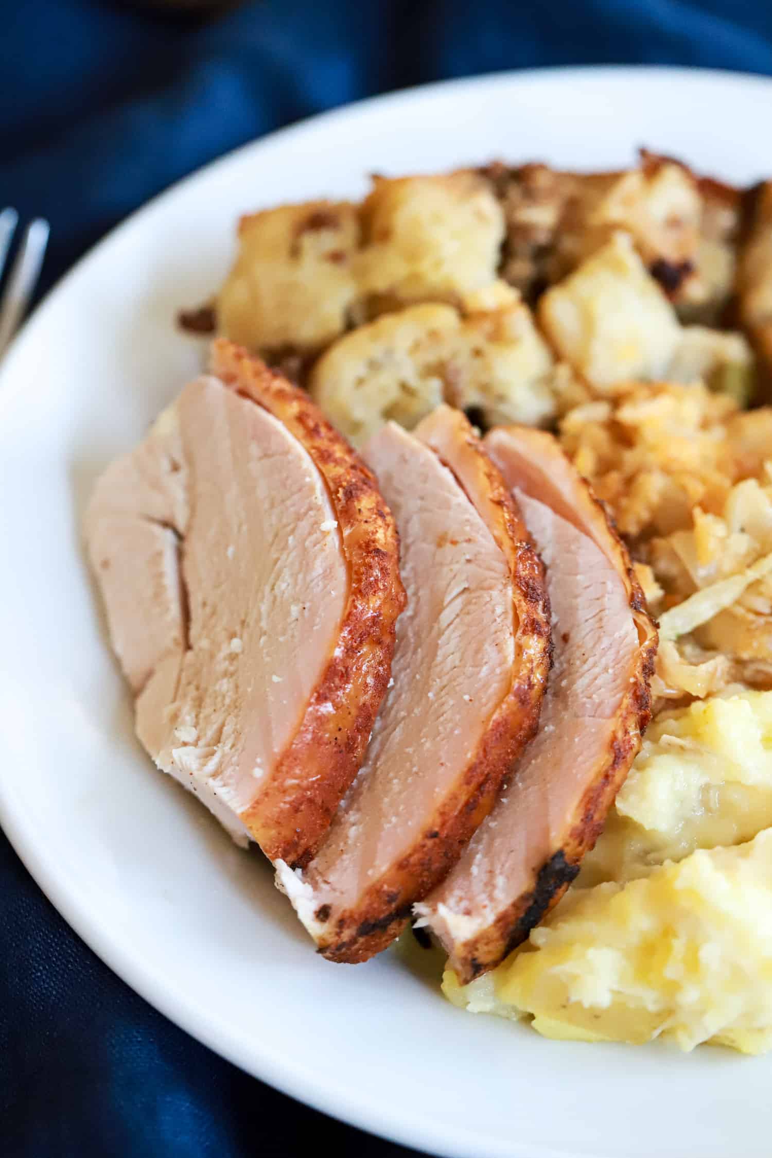 slices of turkey on a white plate with thanksgiving side dishes.