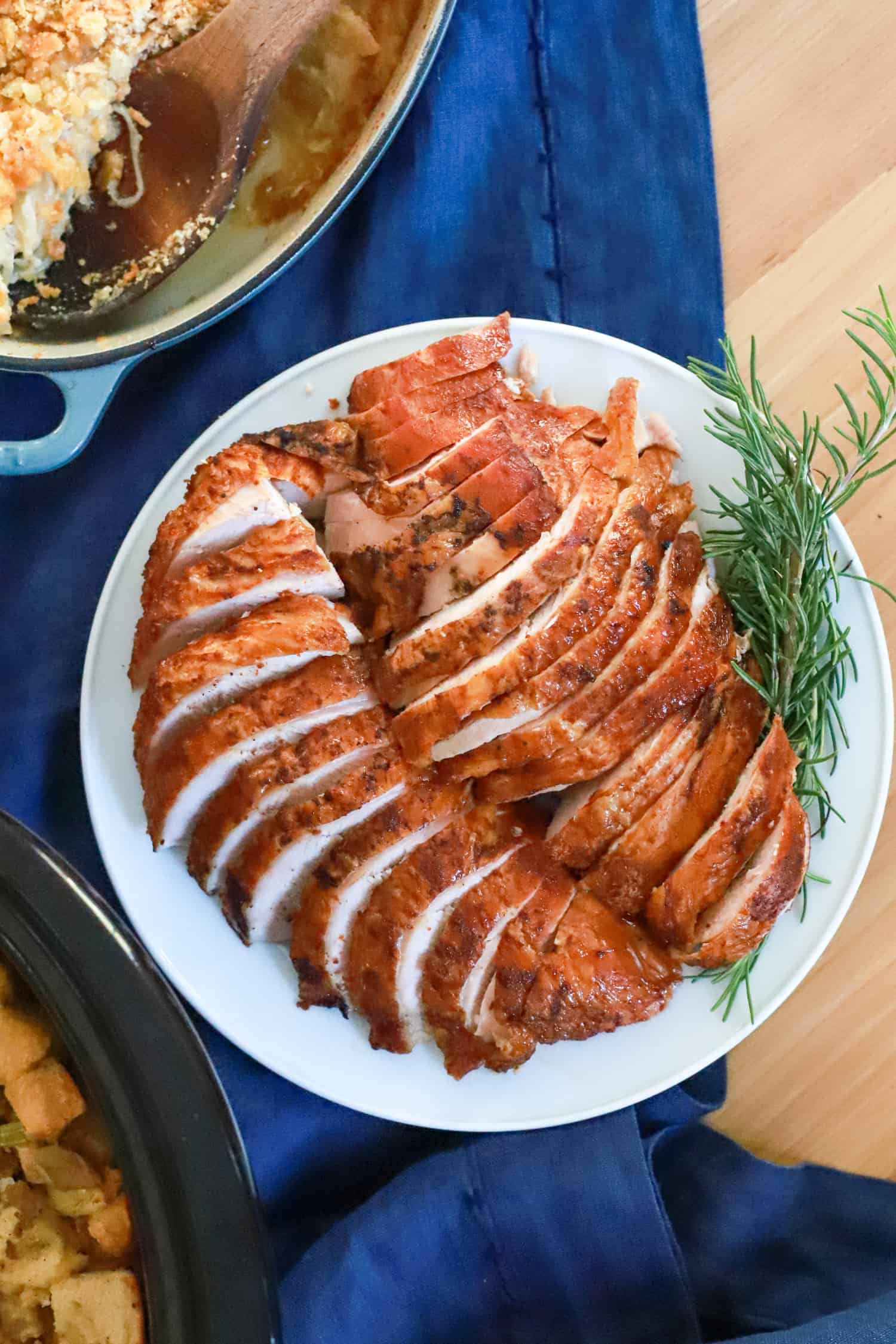 plate of sliced smoked turkey with rosemary garnish on navy blue napkin.