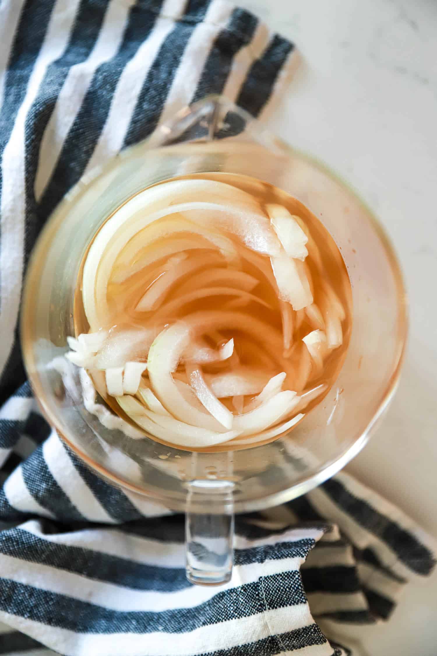 Glass dish of pickled white onions with striped napkin surrounding the dish.