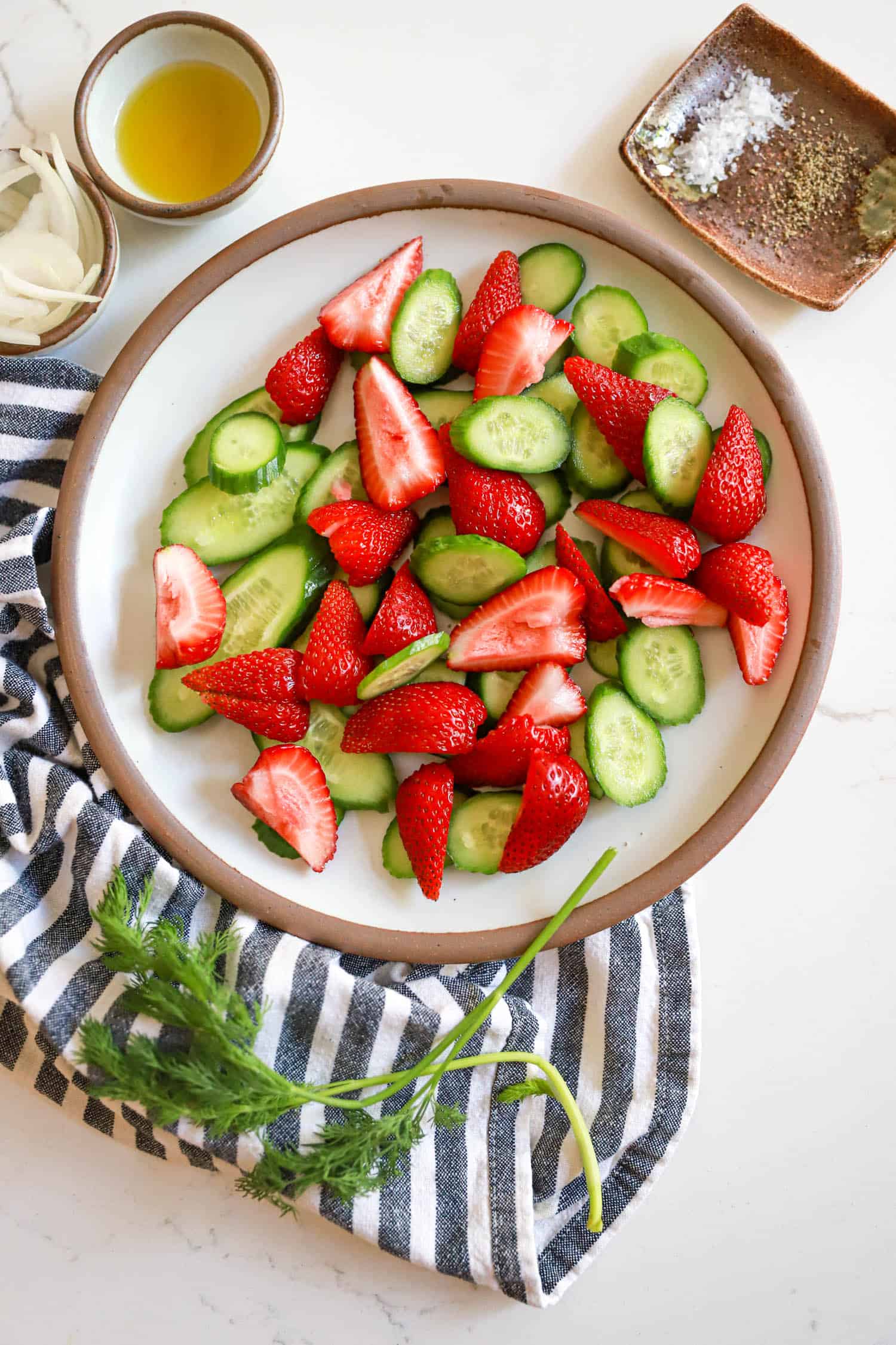 Gray plate of strawberries and cucumbers with fresh dill on the edge.