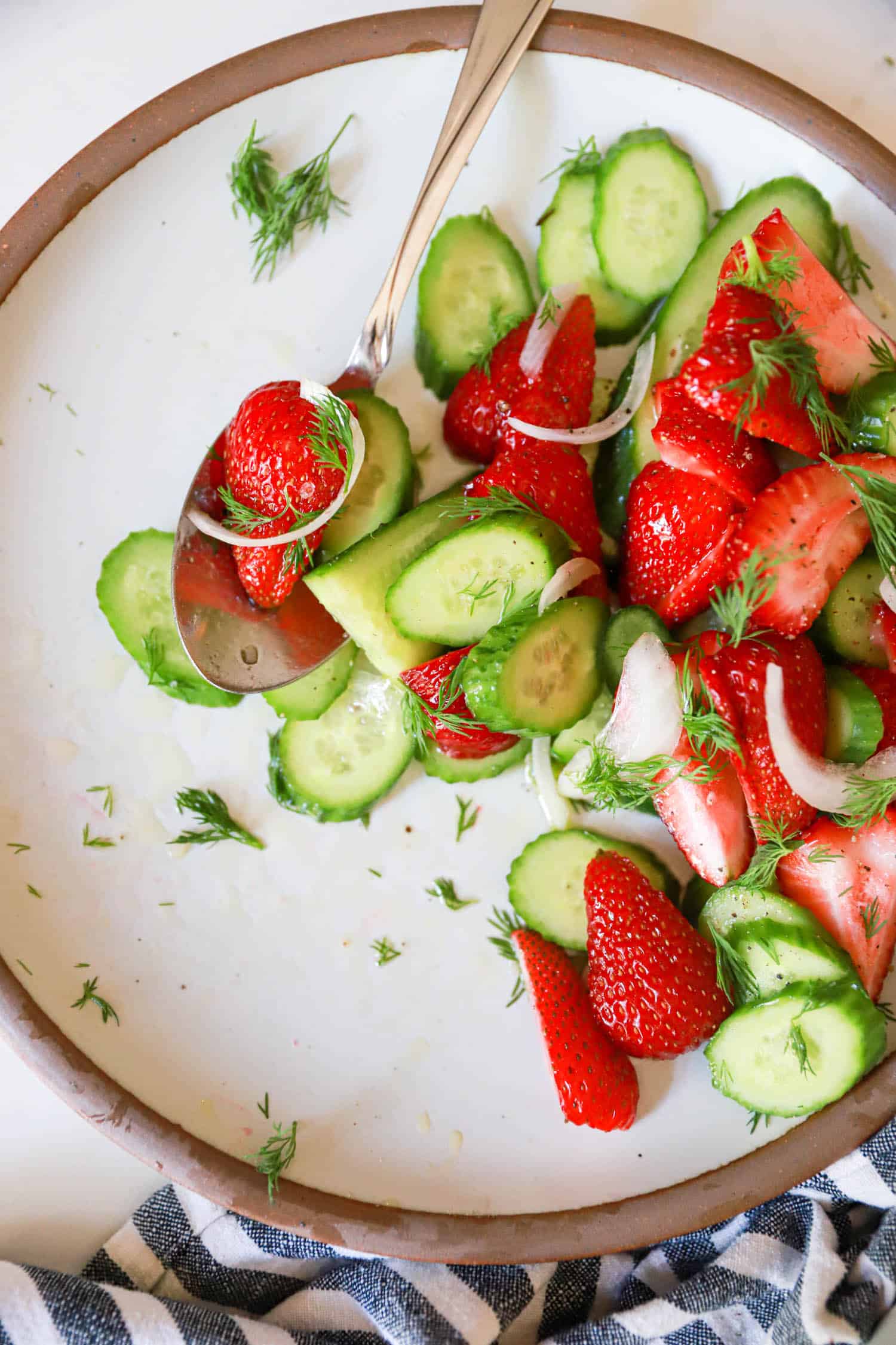 Plate of half eaten strawberry cucumber salad with silver serving spoon.