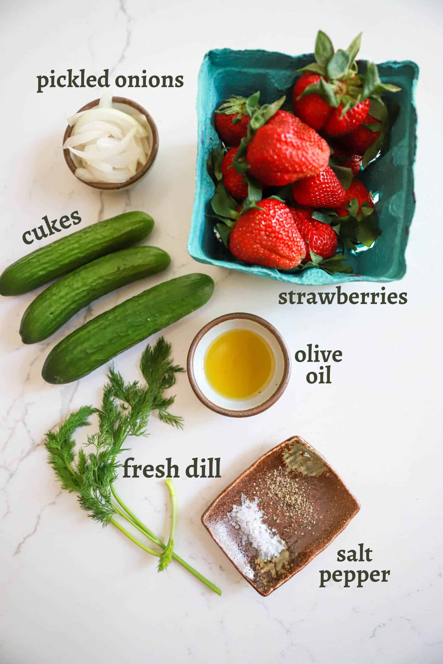 Ingredients for strawberry cucumber salad on white board with labels for ingredient names.