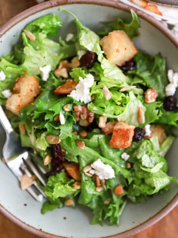 Gray bowl of salad with croutons and goat cheese.